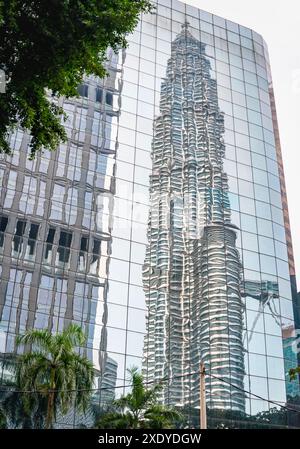 Kuala Lumpur, Malaisie-23 avril 2024 : L'une des tours emblématiques est reflétée par la surface brillante d'une structure vitrée miroir moderne à proximité, donnant un Banque D'Images