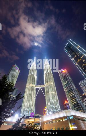 Kuala Lumpur, Malaisie-23 avril 2024 : la nuit, les tours jumelles emblématiques et illuminées et leurs projecteurs réfléchissent la lumière sur les nuages qui passent Banque D'Images