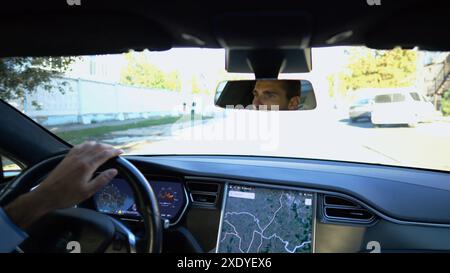 Yeux du conducteur masculin réfléchissant le rétroviseur pendant la conduite d'une voiture électrique. Homme confiant conduisant une voiture moderne en ville. Jeune homme regardant Banque D'Images