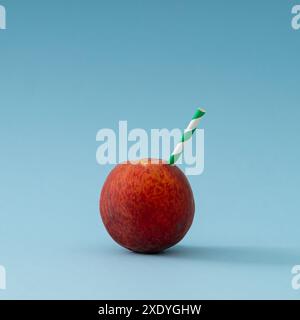 Composition créative faite avec pêche juteuse et paille verte et blanche sur fond bleu clair. Concept minimal de boisson aux fruits d'été. Banque D'Images