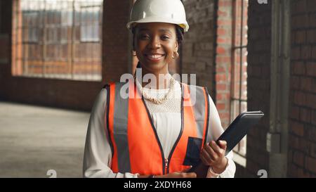 Ingénieur confiant sur le chantier de construction tenant une tablette et portant un équipement de sécurité Banque D'Images
