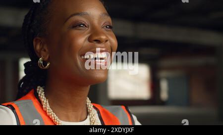 Portrait d'une ingénieure noire souriante dans le chantier de construction portant un équipement de protection Banque D'Images