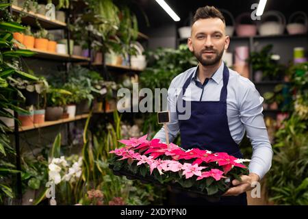 Un vendeur de fleurs dans un salon floristique tient un plateau avec des plantes à fleurs dans ses mains Banque D'Images