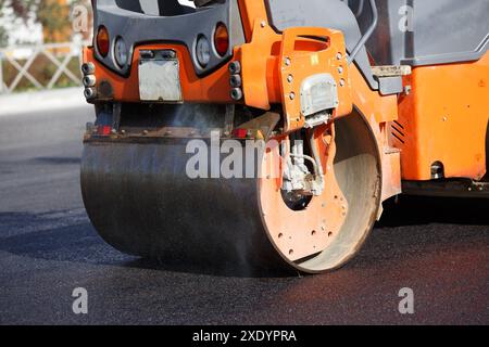 Vue rapprochée du rouleau à vapeur travaillant sur une nouvelle route asphaltée à la lumière du jour d'été Banque D'Images