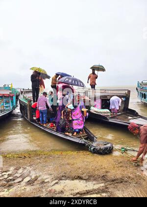 Passagers embarquant et débarquant, sous la pluie tropicale, de lancers de pays qui sont amarrés sur la rive de Dingapotha, Mohonganj «haor» (un grand corps de zone humide formé par la rivière et l'eau de pluie, célèbre comme zone de pêche). Netrokona, Bangladesh. Banque D'Images