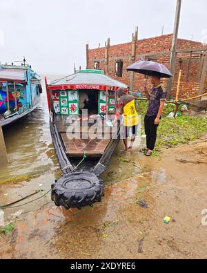 Passagers embarquant et débarquant, sous la pluie tropicale, de lancers de pays qui sont amarrés sur la rive de Dingapotha, Mohonganj «haor» (un grand corps de zone humide formé par la rivière et l'eau de pluie, célèbre comme zone de pêche). Netrokona, Bangladesh. Banque D'Images