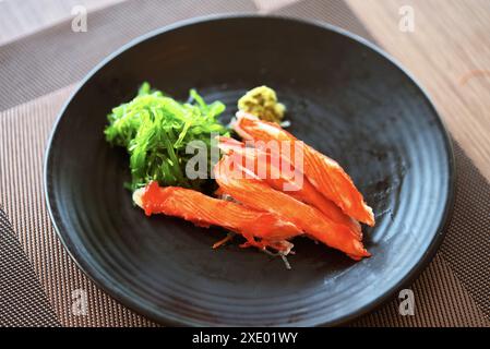 Gros plan sur des bâtonnets de crabe sashimi ou Kani sashimi dans une petite assiette noire avec wasabi et algues. Lumière naturelle de la fenêtre, vue d'en haut autour de 45 degr Banque D'Images