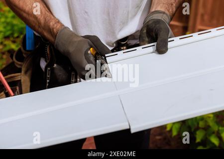 En cours de construction, Craftsman coupe des panneaux de parement en vinyle à la taille désirée avant de les installer Banque D'Images