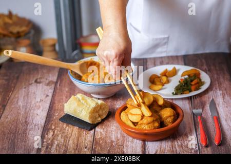 Femme dans un tablier blanc servant des pommes de terre et des légumes sur une portion de boulettes de viande Banque D'Images