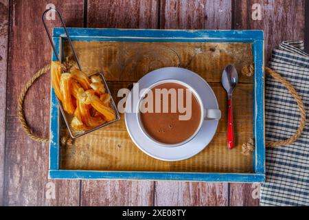 Chocolat chaud dans un mug blanc avec churros dans un plateau en bois bleu Banque D'Images