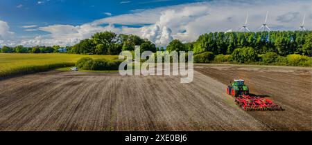 Vue aérienne du tracteur agricole labourant sur le champ agricole avec le parc éolien éolien en arrière-plan. Banque D'Images