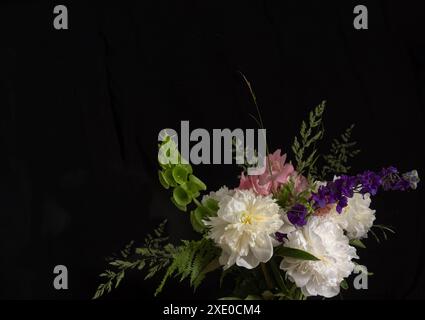 Élégant bouquet de fleurs mélangées comprenant des pivoines blanches, des fleurs roses et violettes et du feuillage vert, disposées sur un fond noir pour un c dramatique Banque D'Images