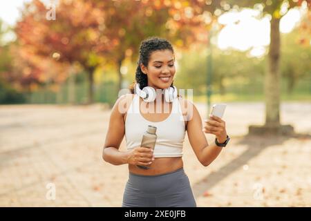 Femme souriante vérifiant son téléphone pendant un entraînement en extérieur Banque D'Images