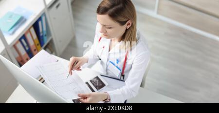 Médecin assis à table et regardant le cardiogramme en clinique Banque D'Images