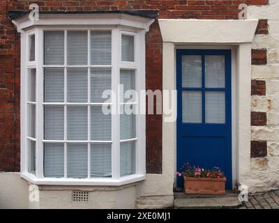 Vue de face d'une vieille maison en brique anglaise typique avec portes peintes en bleu en baie vitrée blanche Banque D'Images