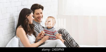 Famille heureuse assise sur Un lit dans Une chambre blanche Banque D'Images