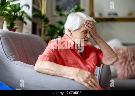 Femme âgée assise dans un fauteuil souffrant de maux de tête Banque D'Images