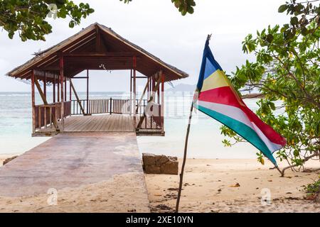 Île de la Digue, Seychelles. Anse Union paysage de plage avec drapeau et un gazebo vide à la jetée sur le fond Banque D'Images