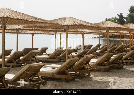 Plage vide avec parasols en paille et chaises longues en bois Banque D'Images