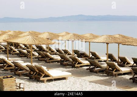 Plage vide avec parasols en paille et chaises longues en bois Banque D'Images