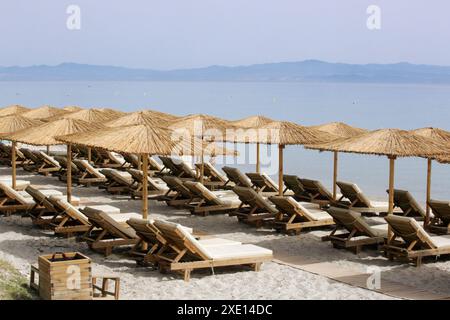 Plage vide avec parasols en paille et chaises longues en bois Banque D'Images