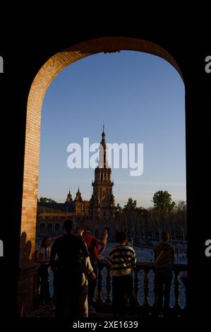 Les gens profitent de la soirée à la Plaza de España à Séville, silhouettée contre la tour historique et le ciel clair, encadrée par une élégante arche en briques Banque D'Images