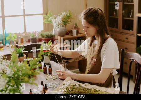 Parfumeur femelle versant de l'eau de rose dans une longue fiole transparente avec un bâton de verre dedans, elle s'est concentrée sur le processus Banque D'Images