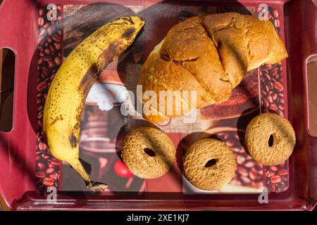 Petit déjeuner sur un plateau avec banane, biscuit avec grains entiers et une brioche au miel. Banque D'Images