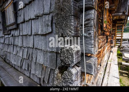 La façade de la Weißalm est revêtue de bardeaux de bois grisés par les intempéries et d’un énorme joint d’angle en troncs, sur le sentier Almenweg dans la vallée de Großarl, Salzbourg, Autriche. Un escalier extérieur en bois mène au niveau supérieur de la cabane centenaire à droite. Banque D'Images