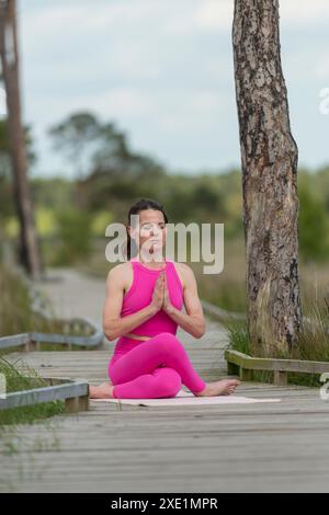 Femme sportive assise sur une promenade méditant et pratiquant le yoga portant des vêtements de sport roses Banque D'Images