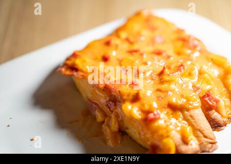 Gros plan d'une tranche de pain pizza au fromage sur une assiette blanche. Le pain est garni de fromage fondu et de petits morceaux de pepperoni. Banque D'Images