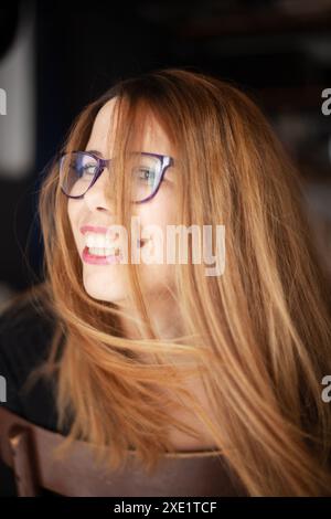 Une image franche capturant une jeune femme joyeuse aux cheveux roux et aux lunettes riant, entourée d'un fond flou. Banque D'Images