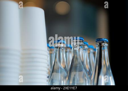 Gros plan de gobelets en papier blanc empilés et de bouteilles en verre avec bouchons bleus. Banque D'Images