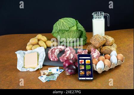 L'épicerie assortie, y compris des légumes, de la viande, des œufs, et un smartphone avec une application de shopping sur une table rustique Banque D'Images