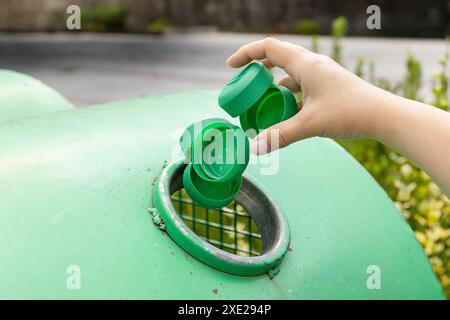 Gros plan d'une main jetant des bouchons en plastique dans un bac de recyclage urbain Banque D'Images