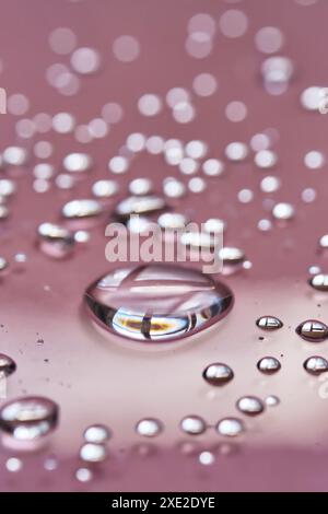 Une grosse goutte et des éclaboussures d'eau micellaire sur fond rose. Banque D'Images