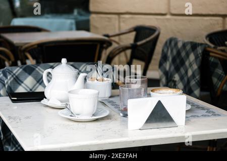 Désordre sur la table avec théière blanche et tasses après le petit déjeuner. Tasse en porcelaine sur la table. Délicieux petit déjeuner délicieux. Restes de nourriture dans des verres sales Banque D'Images