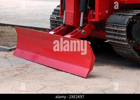 Lame de bulldozer d'un tracteur de construction rouge moderne avec chenilles positionnées sur une surface urbaine en béton en gros plan Banque D'Images