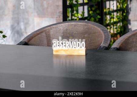 Un panneau en bois avec l'inscription RESERVADO se dresse sur une table avec deux chaises indiquant une place réservée sur la terrasse du restaurant Banque D'Images