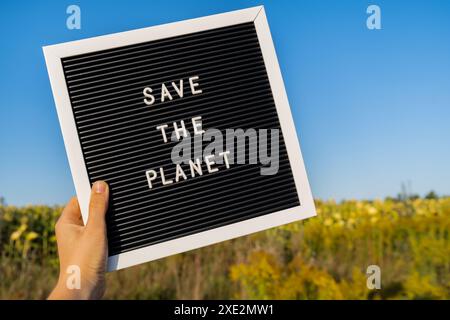 Personne méconnaissable avec message de bannière SAUVER LA PLANÈTE dans le champ de tournesol le jour ensoleillé. Signe jour de LA TERRE. Concept d'écologie an Banque D'Images