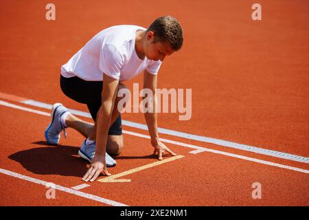 Un athlète déterminé est accroupi à la ligne de départ d'une piste rouge, prêt à commencer une course de sprint Banque D'Images