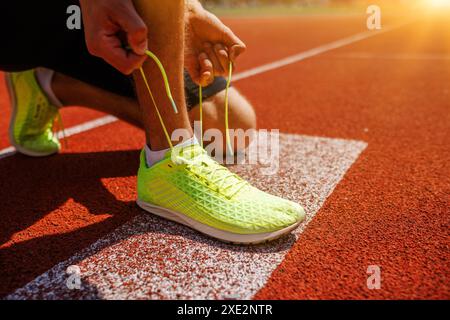 Un athlète est en train de lacer des chaussures de course jaune fluo vif sur une piste, se préparant pour une course au lever du soleil Banque D'Images
