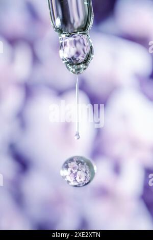 Une goutte d'huile cosmétique tombe de la pipette sur un fond floral violet. Banque D'Images