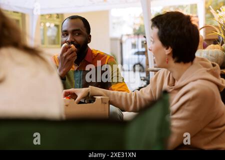 Jeune homme noir mordant une pomme biologique fraîche au festival de dégustation de nourriture en plein air. Couple multiculturel dégustant et dégustant divers fruits et légumes cultivés localement au marché des agriculteurs. Banque D'Images