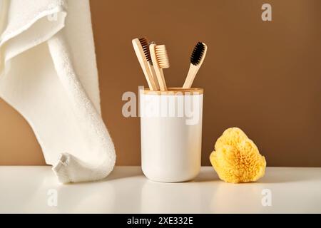 Brosses à dents en bambou dans une tasse et une serviette dans un intérieur de salle de bain. Banque D'Images