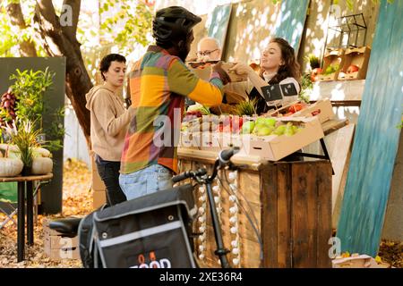 Livreur africain debout près du marché agricole se tient ramasser la boîte de produits biologiques frais. Black Guy Courier livrant des fruits et légumes bio produits par les agriculteurs locaux aux clients. Banque D'Images