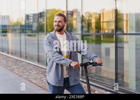 Jeune homme chevauchant son e-scooter dans la rue de la ville Banque D'Images