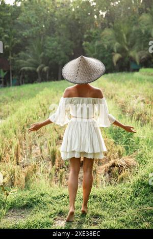 Femme portant des vêtements naturels et chapeau conique asiatique dans le champ de riz pendant le coucher du soleil Banque D'Images