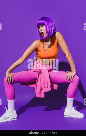 Jeune danseuse insouciante portant des vêtements de sport colorés exécutant sur fond violet Banque D'Images