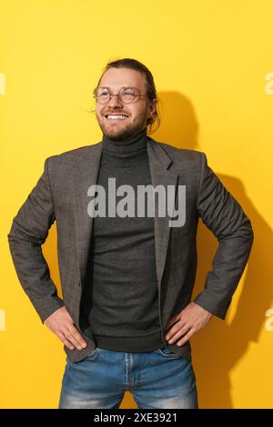 Bel homme barbu portant des lunettes souriant sur fond jaune Banque D'Images